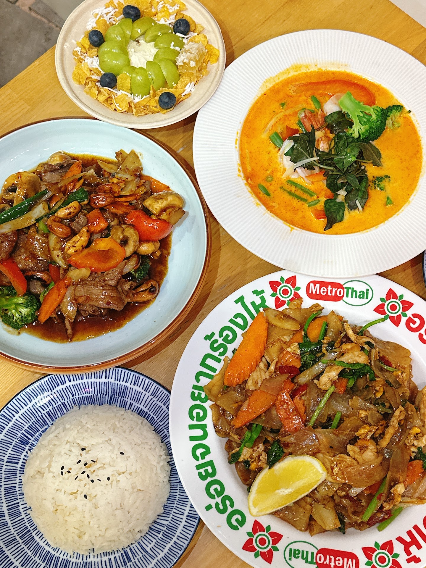 Metro Thai table spread with fried rice, skewers, Thai dishes, drink, and fruit bowl